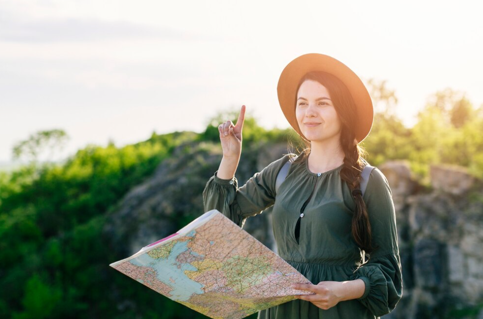 woman tourist in a green dress and hat holding the map among rocky landscape